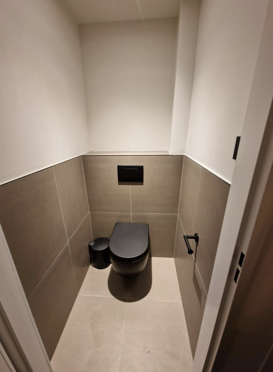 Kleine toiletruimte met zandkleurige wandtegel en zwart hangtoilet